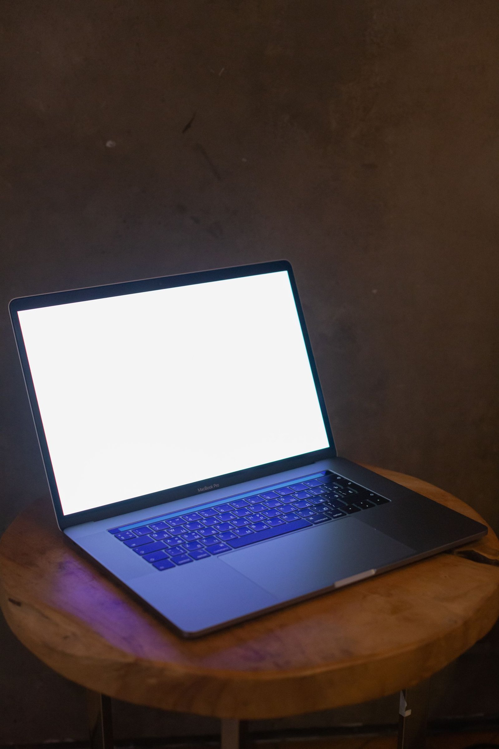 Photo of a laptop with a blank screen illuminated in a dim room on a wooden surface.